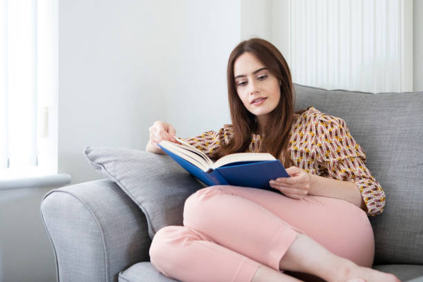 istock One young woman relaxing on a sofa and reading a book 1332443208