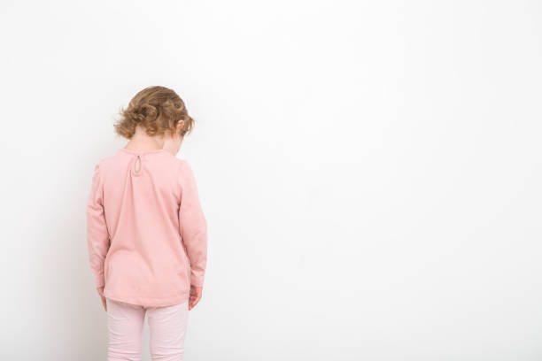 kleines mädchen in rosa kleidern, das auf weißem wandhintergrund steht. bestraftes kleinkind. rückansicht. leerer platz für text. - violence child abuse child baby girls stock-fotos und bilder