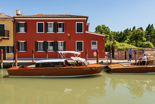 Torcello, Italy - June 2th, 2021: Two traditional water taxis made of wood moored in a small canal in Torcello island, Venetian lagoon, Venice, UNESCO world heritage site, Veneto, Italy, Europe. Two taxi drivers await their customers on a sunny spring day.