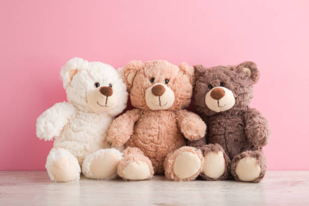 smiling white, light brown and dark brown teddy bears sitting on table at pink wall background. pastel color. togetherness and friendship concept. front view. closeup. - speelgoedbeest stockfoto's en -beelden