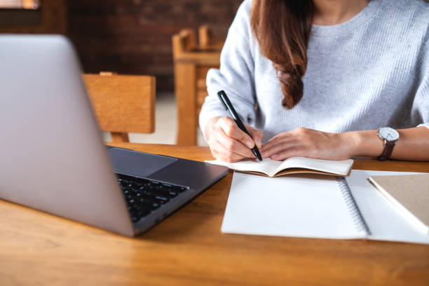 istock a woman writing on a notebook while working on laptop computer in office 1332456351