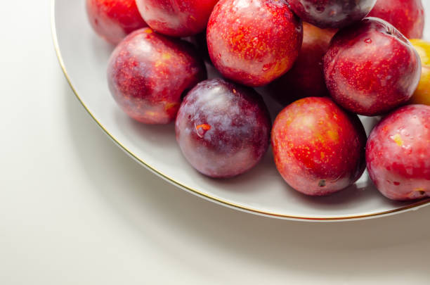 istock Closeup on fresh and ripe plums on a white ceramic plate 1332460420