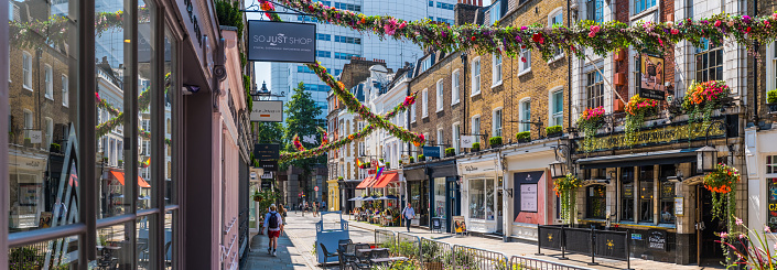 Flower garlands decorating a pedestrianised shopping street of independent stores in Covent Garden Soho, London, UK.