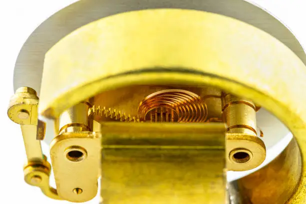 Macro photo of a bourdon tube pressure gauge mechanism with exposed copper elements, isolated on a white background.