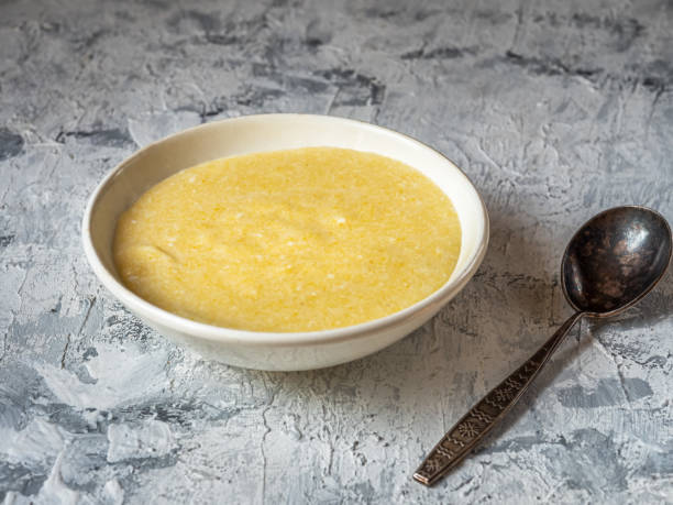 porridge di mais sul latte in un piatto bianco su sfondo chiaro - polenta cooking food spoon foto e immagini stock