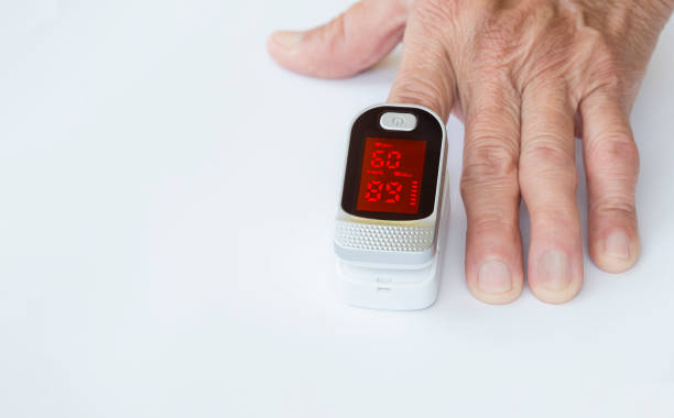 фокусировка на пульсоксиметре на указательном пальце пожилой руки на белой столешницы - taking pulse oximeter medical oxygen equipment human lung стоковые фото и изображения