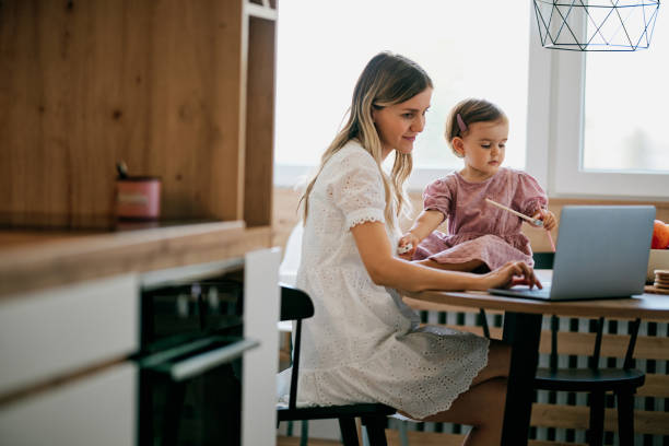 istock Stay at mother home sitting in kitchen and getting work done while her baby girl helping her. 1332473044