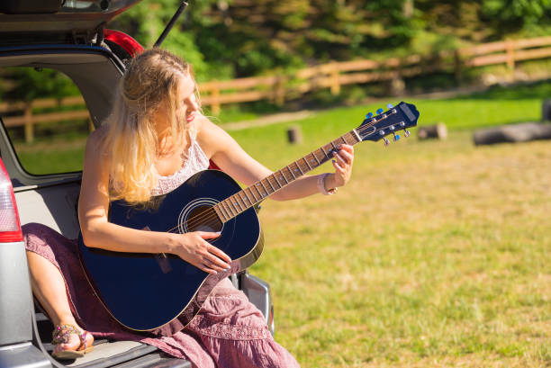 istock Hippie woman playing guitar in van car 1332476484
