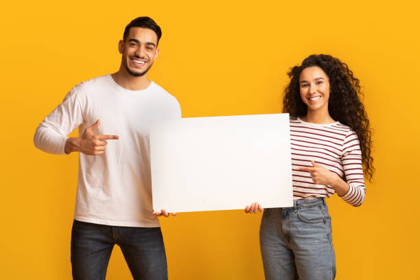 istock Happy Middle Eastern Couple Pointing At Blank White Placard In Hands 1332476907