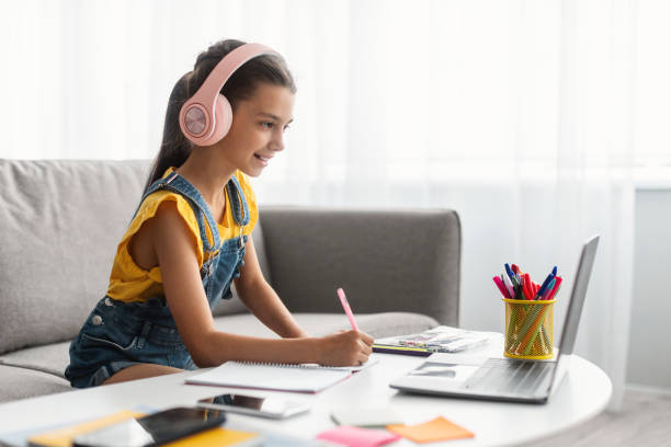 istock Girl sitting at desk, using laptop, writing in textbook 1332477058