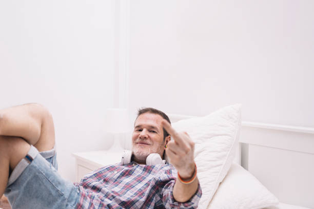 istock man lying in bed, looking at the camera and raising his middle finger on his hand 1332477193