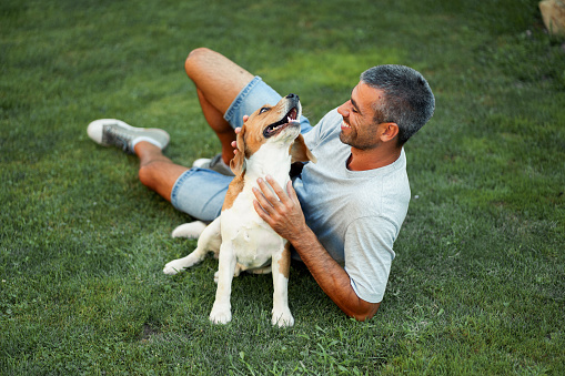A young men is playing and cuddling with his dog on the lawn.