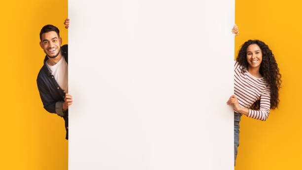 istock Cheerful Young Arab Couple Standing Near Big White Advertisement Board 1332478558