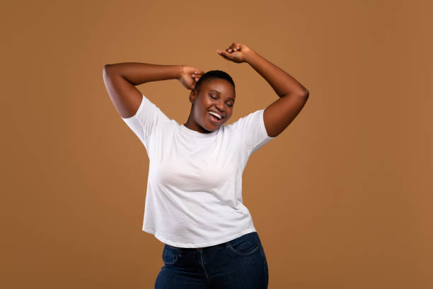 portrait of casual young black woman dancing, brown wall - plussize model fotos stockfoto's en -beelden