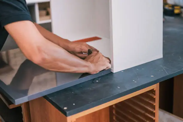 Photo of Hands of a man fixing a hinge on a surface for a kitchen.