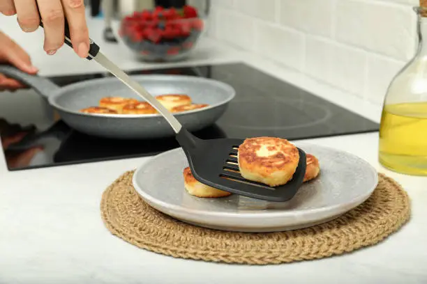 Woman frying delicious cottage cheese pancakes in kitchen, closeup
