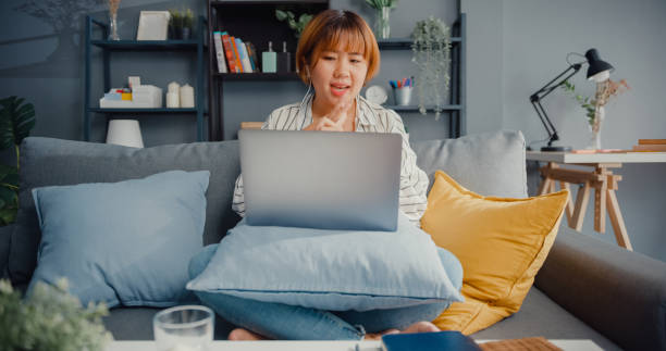 istock Asia businesswoman using laptop talk to colleagues about plan in video call while working from house at living room. 1332482038