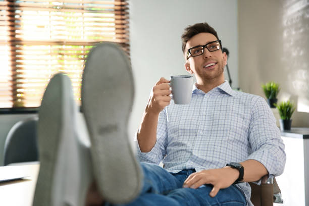 istock Young man with cupa of drink relaxing at workplace 1332482257