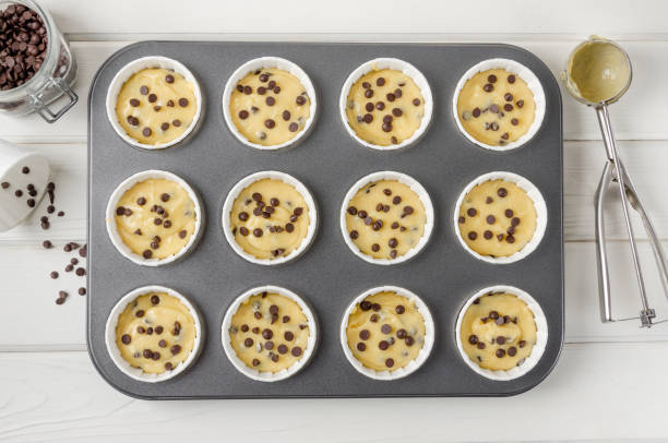 Raw dough for muffins with chocolate chips in baking form on a white wooden background. Recipe step by step. Top view.