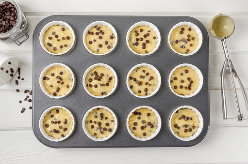 Raw dough for muffins with chocolate chips in baking form on a white wooden background. Recipe step by step. Top view