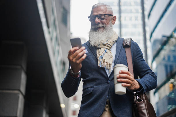 istock Business hipster senior man using mobile phone while walking to work with buildings in background - Focus face 1332483778