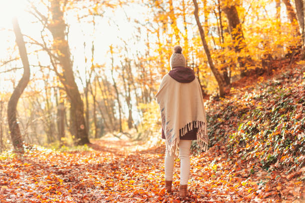 istock Woman walking down colorful autumnal forest path covered with fallen leaves 1332484100
