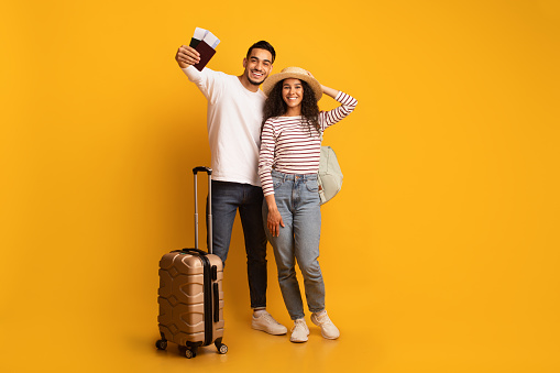 Vacation Finally. Portrait Of Happy Arab Tourist Couple With Passports And Suitcase Posing Over Yellow Background In Studio, Joyful Excited Middle Eastern Spouses Ready For Family Trip, Copy Space