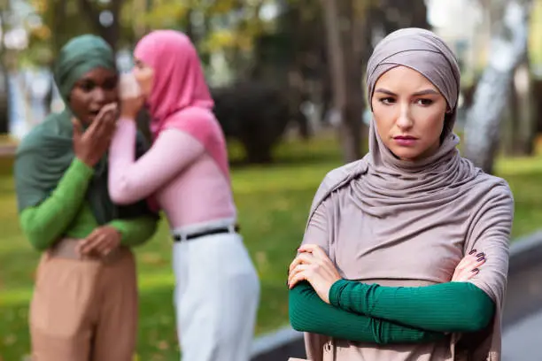 Photo of Islamic Ladies Whispering Behind Back Of Their Unhappy Friend Outdoors