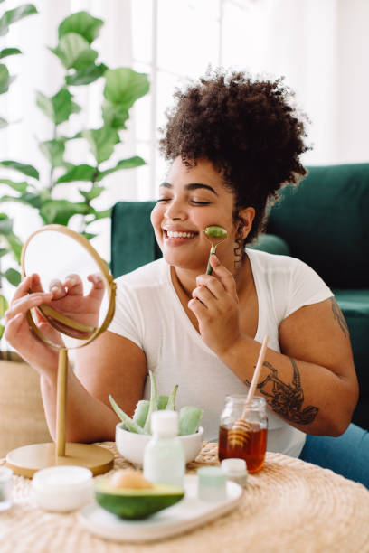 Woman doing self beauty care treatment at home Pretty female using jade roller on face skin for smoothing at home. Woman doing self beauty care treatment at home. body care stock pictures, royalty-free photos & images