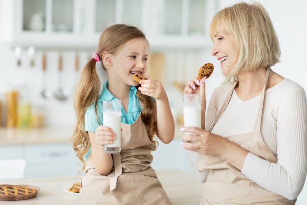 urocza mała dziewczynka i jej babcia jedzenie ciasteczka picie mleka - morning breakfast cookie sweet food zdjęcia i obrazy z banku zdjęć