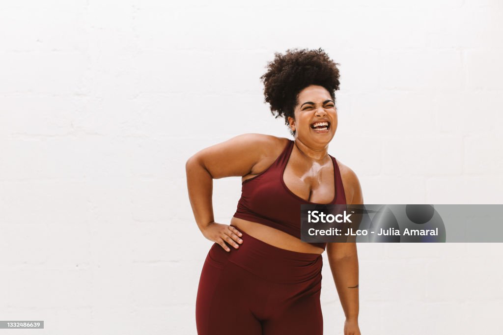 Woman sportswear relaxing after exercise Plus size woman smiling with closed eyes with one hand on her waist. Pretty female in sportswear relaxing after exercise on white background. Women Stock Photo