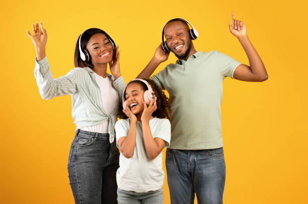 enjoy music together. happy african american family of three dancing in headphones, isolated on yellow background - parent mother music listening imagens e fotografias de stock