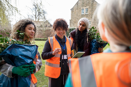 Medium shot of women working together on a community garden outreach project to help improve their local environment. They are wearing hi-vis jackets as they stand together using a Digital tablet, discussing their plan of action in the North East of England.