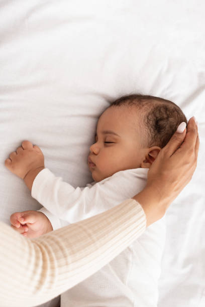 istock Black Mom's Hand Stroking Sleeping Baby's Head In Bed, Cropped 1332489480