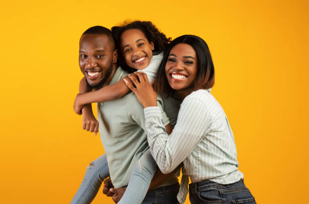 Time with family. Overjoyed african american family laughing and posing to camera isolated over yellow studio wall Time with family. Overjoyed african american family laughing and posing to camera isolated over yellow studio wall. Cheerful father carrying his daughter on back excited woman yellow stock pictures, royalty-free photos & images