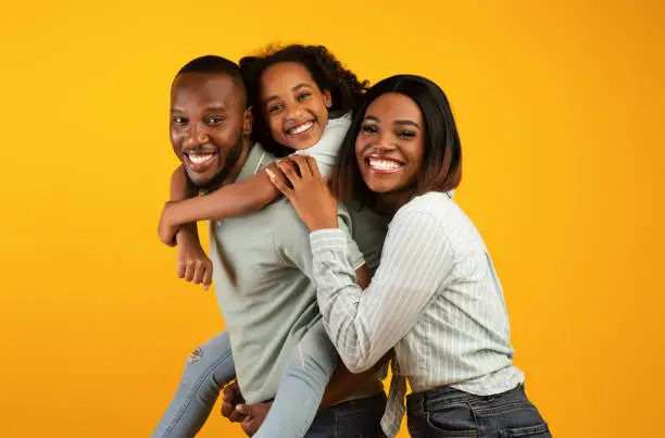 Photo of Time with family. Overjoyed african american family laughing and posing to camera isolated over yellow studio wall