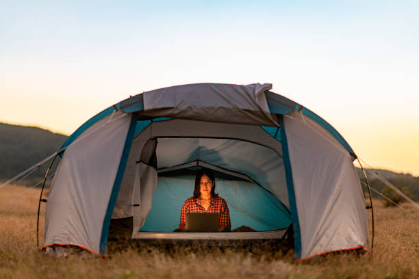 istock Young woman using laptop next to her tent while camping in nature 1332495850