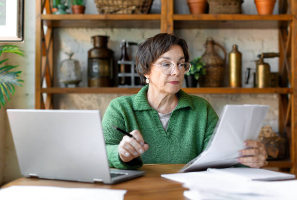 A mature woman during a document check. She checks the correctness of filling out the documentation and enters the data on the site stock photo