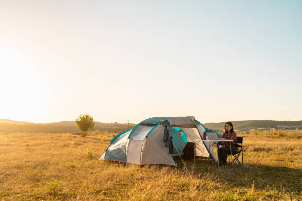 istock Young woman using laptop next to her tent while camping in nature 1332499065