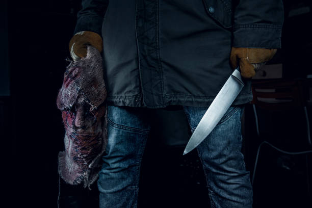 istock Murderer holding on a mask and a knife in the dark spooky room. 1332499343