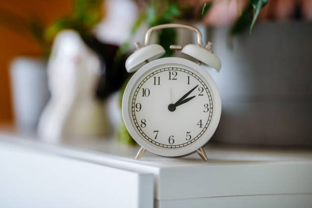 istock White alarm clock on the shelf with home plants 1332499869