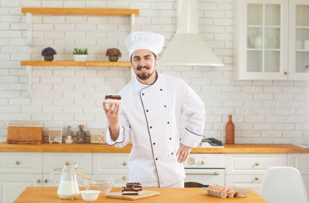 istock Confectioner man smiles while standing with cake in his hands at the kitchen bakery 1332500770