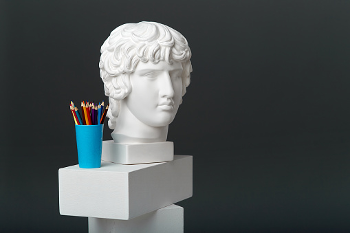 Antinous ' plaster head stands next to a set of pencils in a glass. Concept of drawing and creative activities.
