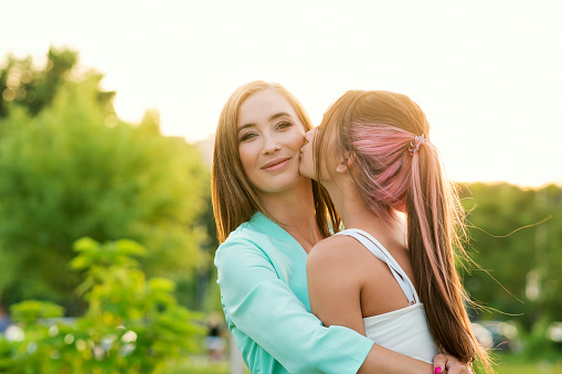 Teen Daughter Kissing on Cheek Smiling Mother. Enjoying moment and Having Fun Together. Candid Portrait Unrecognizable Teenage Girl and Mom.