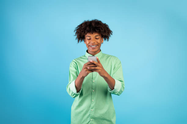 istock People and gadgets. Happy black guy using smartphone browsing internet standing over blue studio background 1332517729