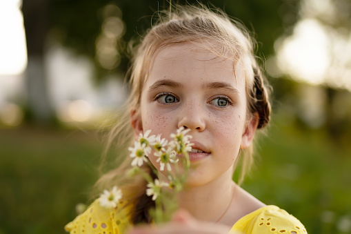 An eight years old freckled face girl in a yellow dress with camomile