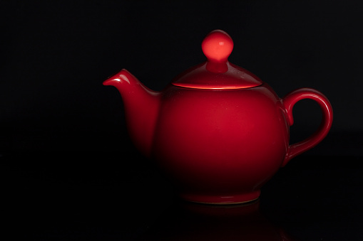 Teapot of red color of the classical form on a black background.