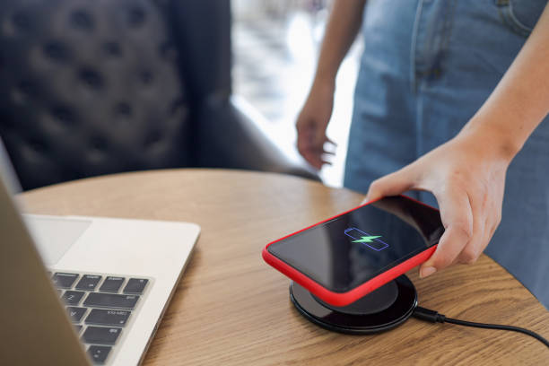 istock Charging mobile phone battery with wireless device in the table. Smartphone charging on a charging pad. Mobile phone near wireless charger. 1332521703