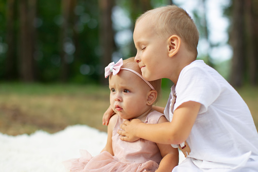 The older brother hugs his little sister for a walk in the park.