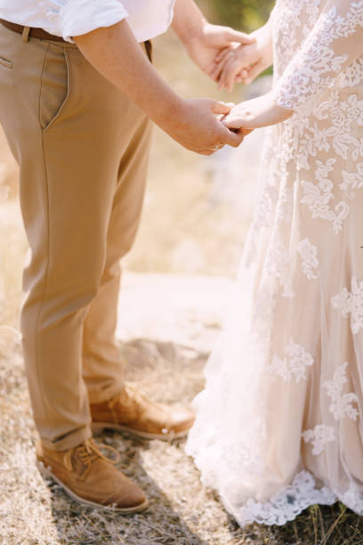 istock Groom and bride stand holding hands on grass. Close-up 1332528511